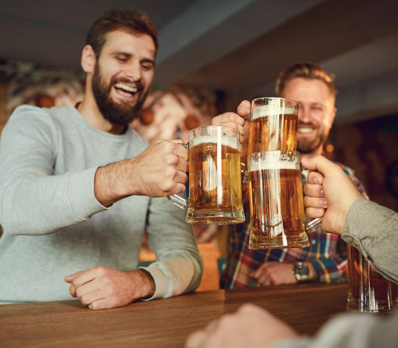 Three men at a bar cheerfully clinking large mugs of beer together.