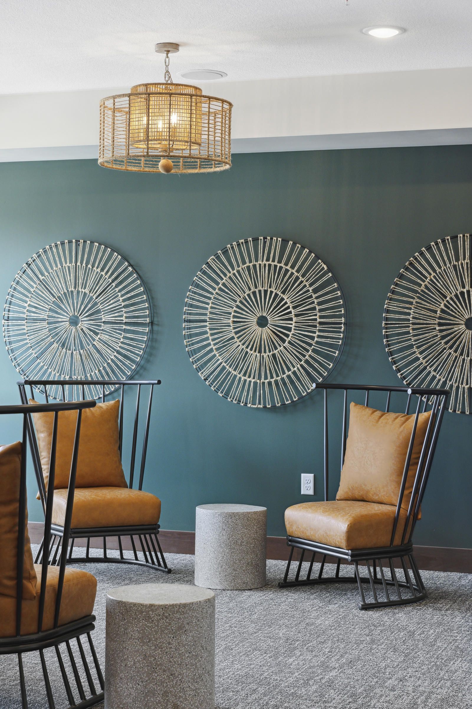 Modern lounge with brown chairs, round wall art, a woven light fixture, and cylindrical stone tables.