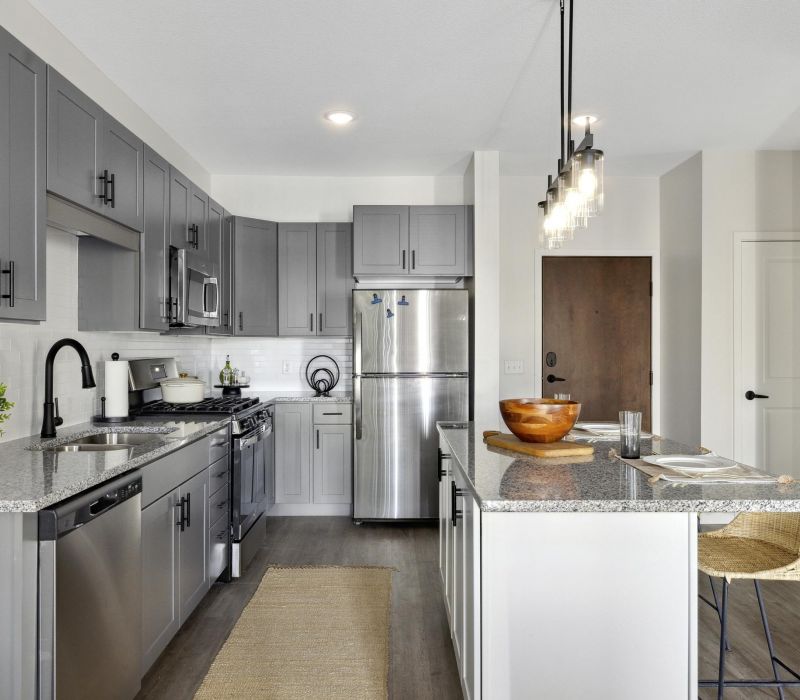 Modern kitchen with gray cabinets, stainless steel appliances, and a breakfast bar with stools.