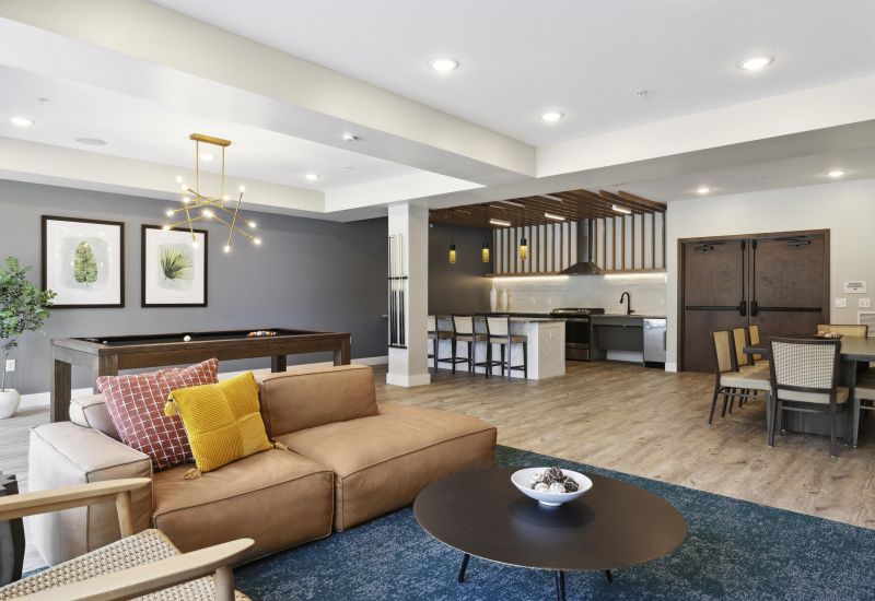 Modern open-concept lounge with sofa, pool table, kitchen, dining area, and contemporary lighting.