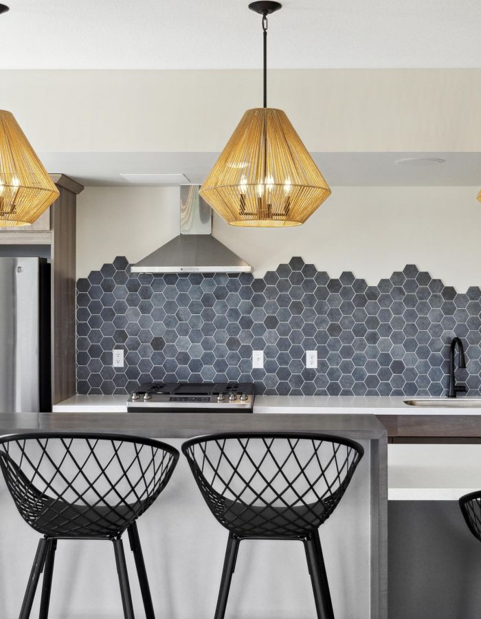Modern kitchen with black hexagon tile backsplash, three pendant lights, and black wire bar stools at an island.
