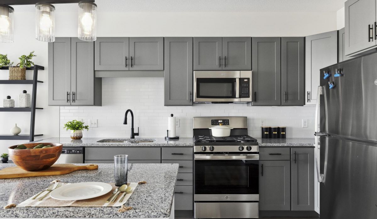 Modern kitchen with gray cabinets, granite countertops, stainless steel appliances, and a set dining island.