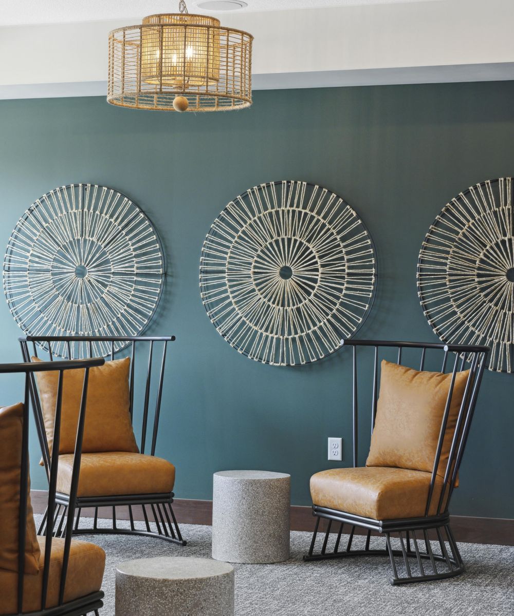 Modern lounge with brown chairs, round wall art, a woven light fixture, and cylindrical stone tables.