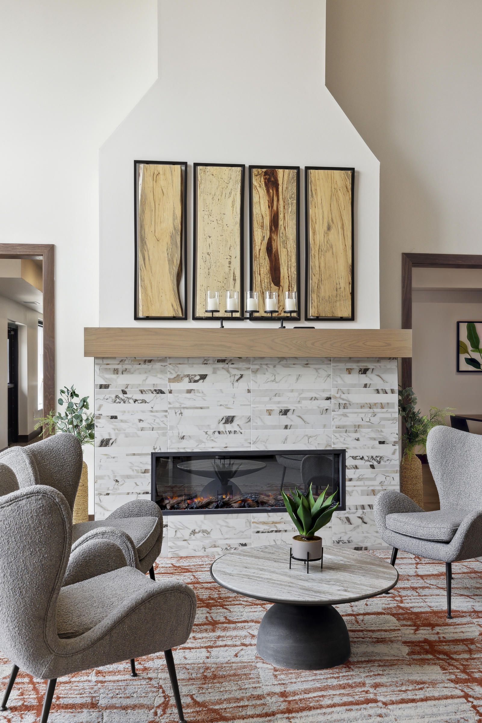 Modern living room with gray chairs, marble fireplace, abstract art, and a round coffee table with a plant.