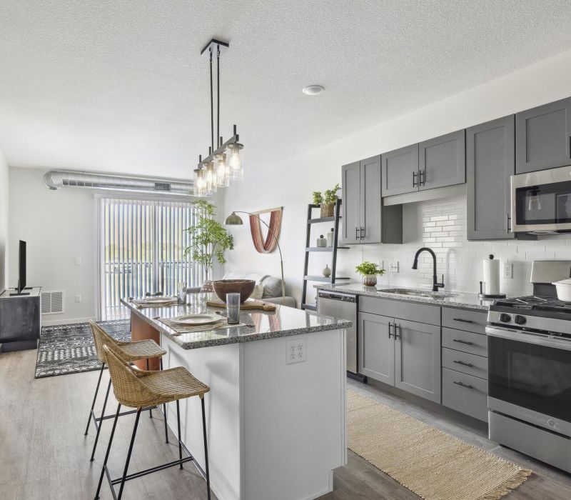 Modern kitchen with gray cabinets, island seating, stainless appliances, and open living area with natural light.