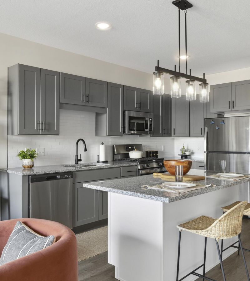 Modern kitchen with gray cabinets, island seating, stainless steel appliances, and decorative open shelving.