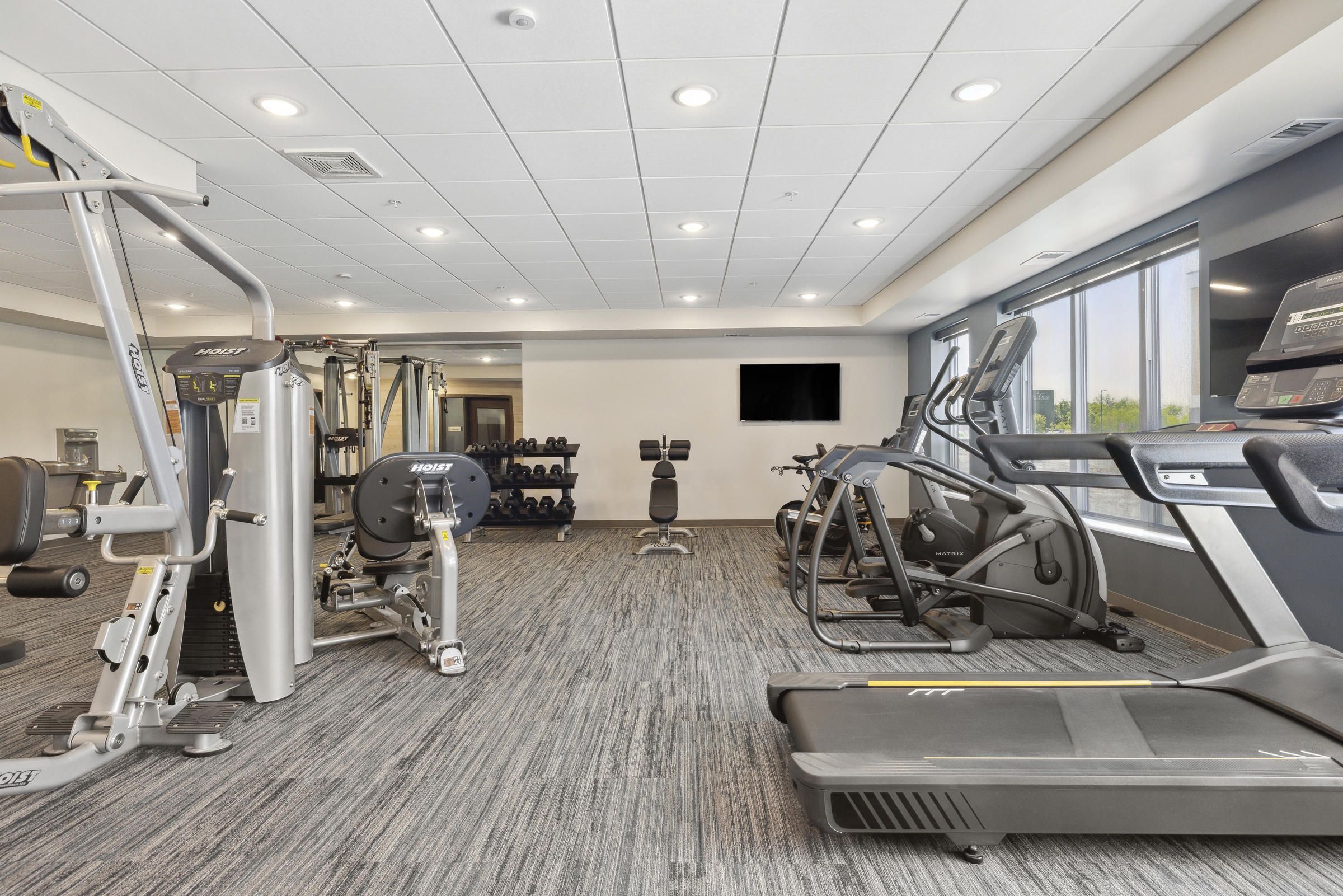 Modern gym with treadmills, elliptical machines, weight machines, and free weights in a bright, spacious room.